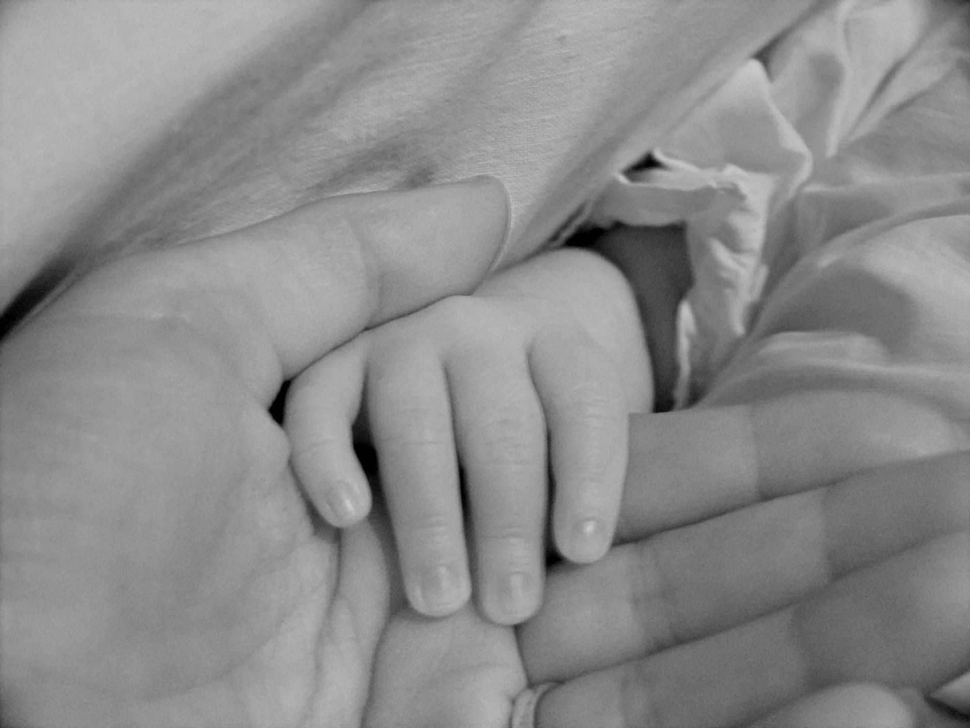 Main d'un nourrisson saisissant le doigt d'un adulte pour illustrer "retrouver la date de naissance d'un ancêtre".